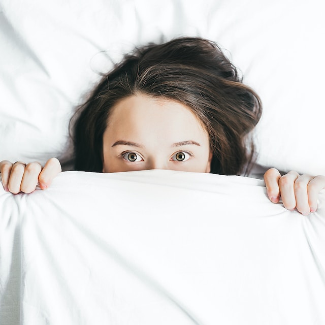girl in bed with covers pulled up over half her face